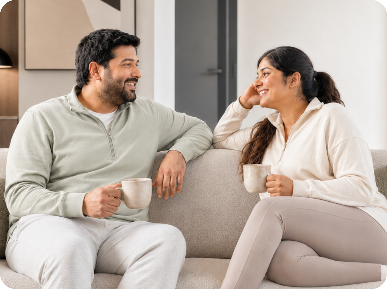 A couple sitting together on a sofa with mugs of tea, talking and smiling